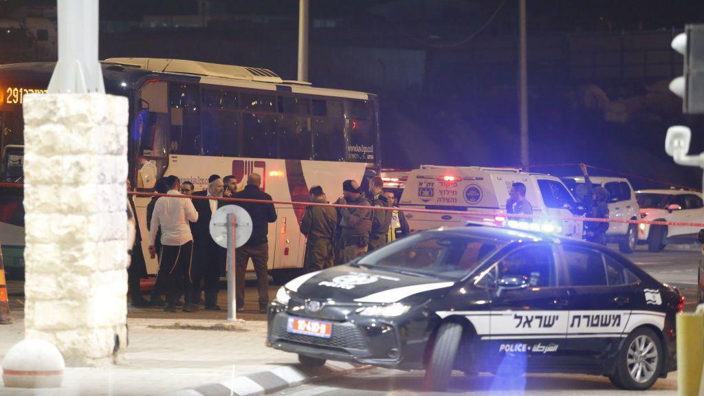 Israeli forces stand near a bus that was attacked by a Palestinian gunmen, killing an Israeli boy, at the Tunnel Military Checkpoint between Jerusalem and the West Bank city of Bethlehem (12 December 2024). A police car with blue light is in the foreground