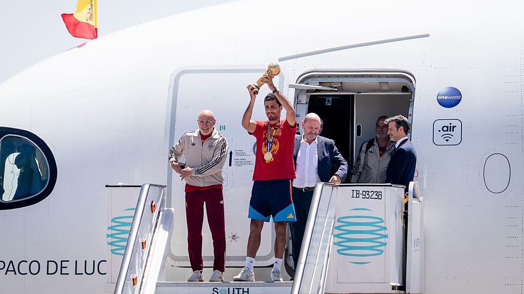 Rodri lifts the World Cup trophy at the top of the aeroplane steps