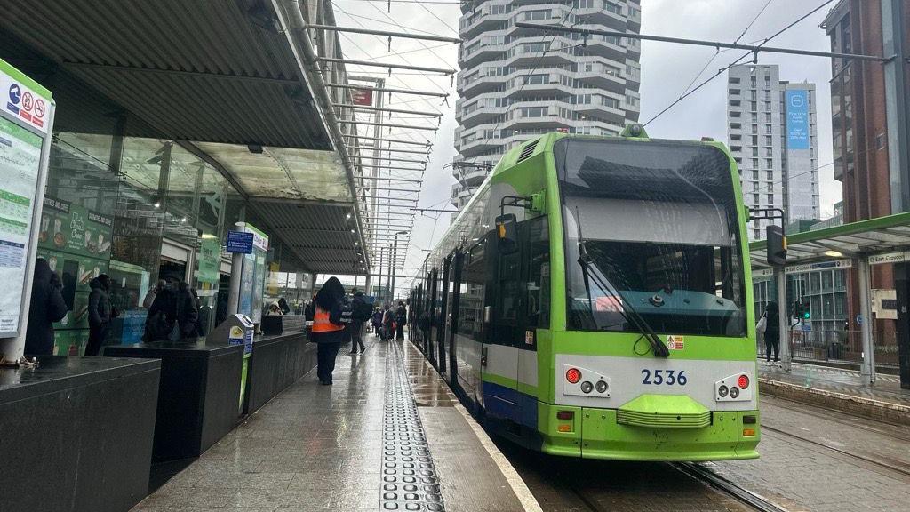 A green tram at a tram station in London. 
