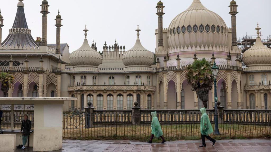 People in rain ponchos walking by the Royal Pavilion in Brighton