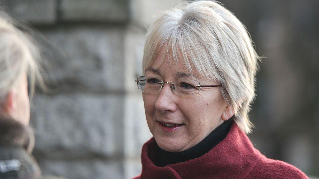 Mary Hanafin looking to her right. she is wearing a burgundy coat and glasses. She has light hair.
