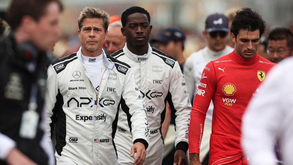 Actor Brad Pitt in a racing uniform and then Ferrari driver Carlos Sainz to his right as scenes for the F1 movie are filmed during the 2023 grand prix at Silverstone