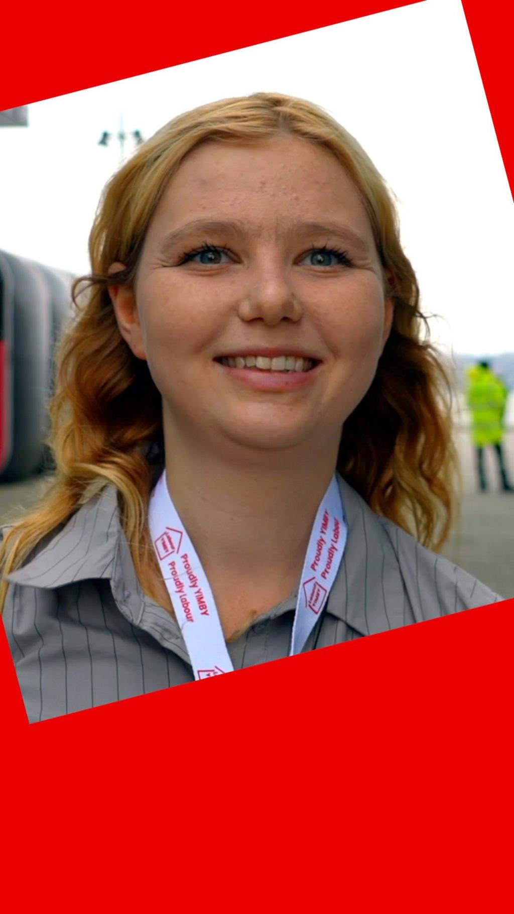 A woman smiles - she has blonde hair and wears a grey shirt