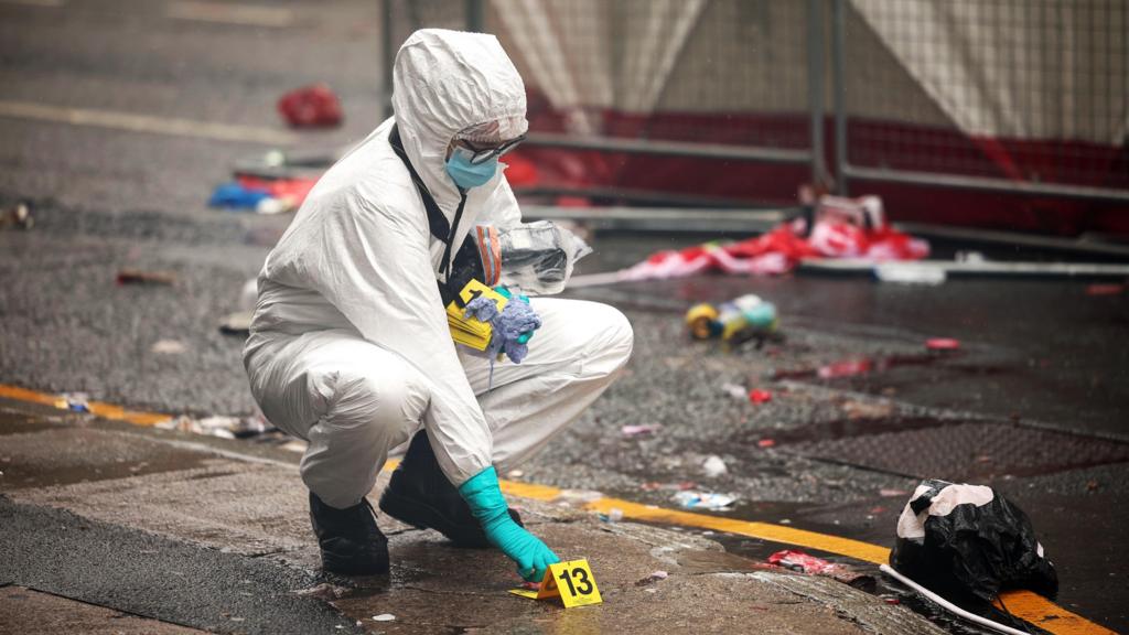 A forensic officer puts down a marker sign on the pavement