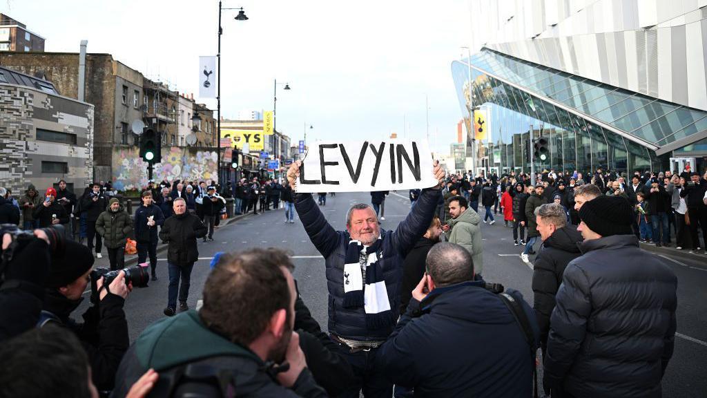 A single counter-protester holding a sign saying "Levy in" aloft above his head