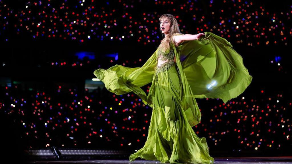 Taylor Swift in a flowing green dress during her Eras Tour on stage