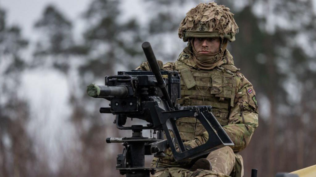 A British soldier sits on top of a vehicle behind a mounted machine gun 