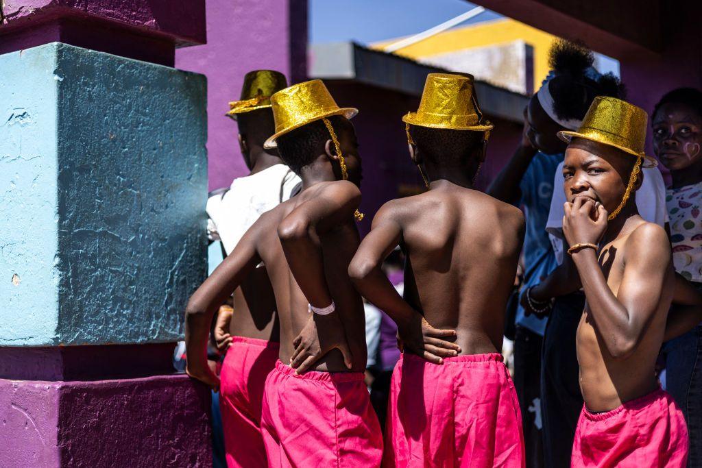 Boys dressed in pink trousers and gold hats stand together.