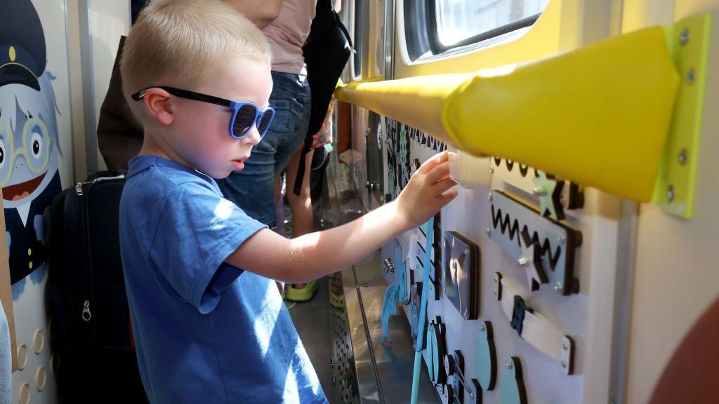 a special children's carriage on a train in Ukraine. A boy in a blue t-shirt plays with a busy board in the train carriage.