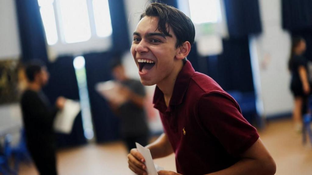 Student in a red top smiles holding a paper.