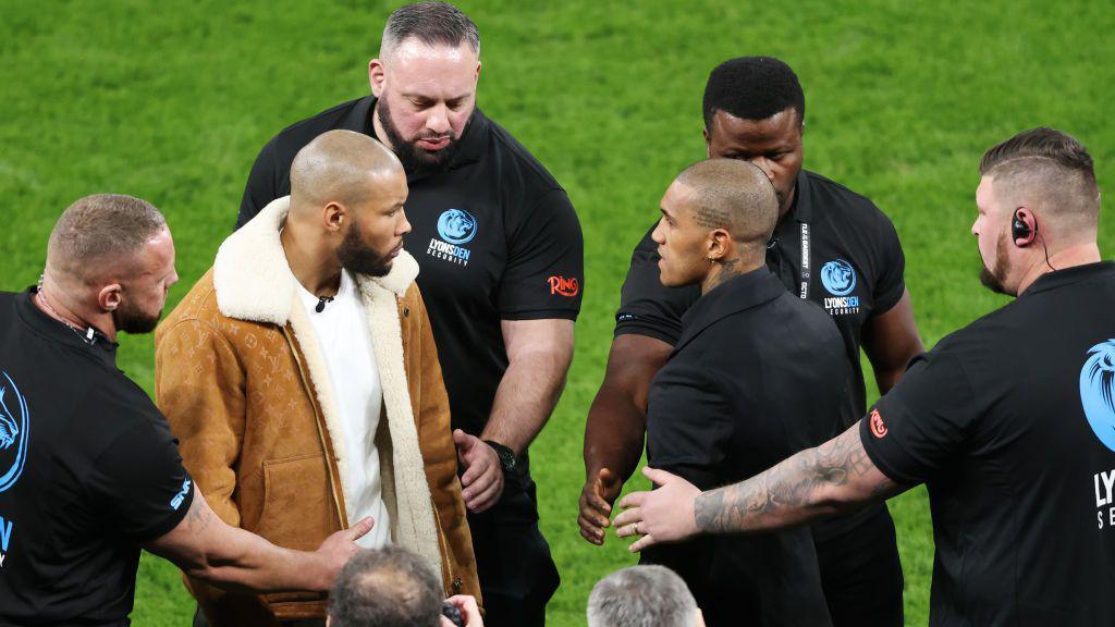 Chris Eubank Jr and Conor Benn facing off on the pitch at Tottenham Hotspur Stadium and separated by security men