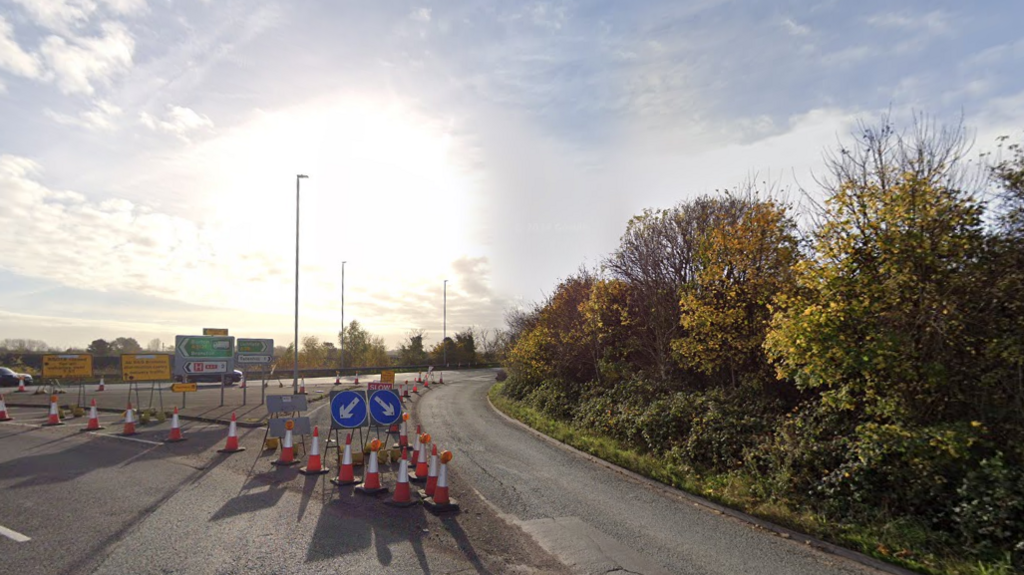 A large roundabout with traffic cones and blue road signs across the left hand lane