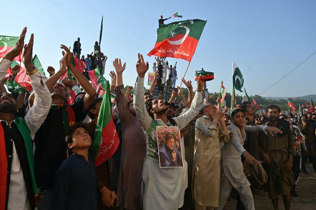 Men, women and children look to the sky and raise their hands while flags wave overhead