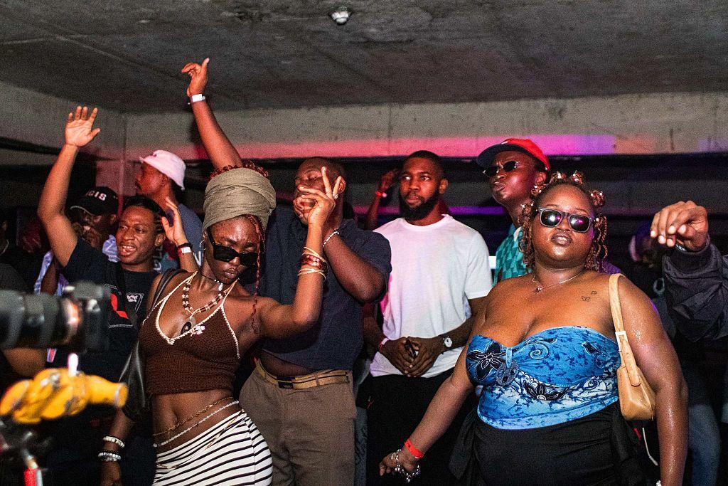 Men and women dance inside a club. Out of shot is a DJ playing music on decks.