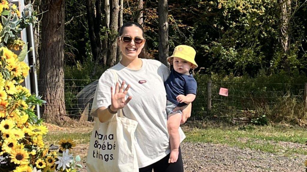 Llun o Helen yn gafael ei mab yn yr haul, o dan forder o flodau haul.