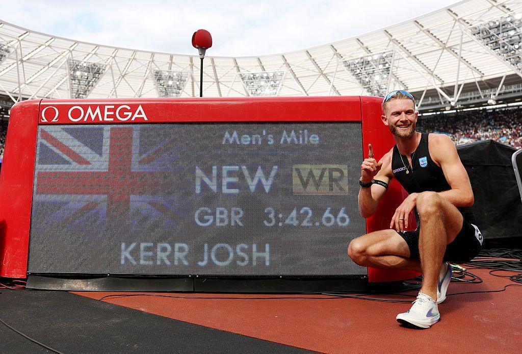 Josh Kerr kneels in front of a sign showing his World Record time.