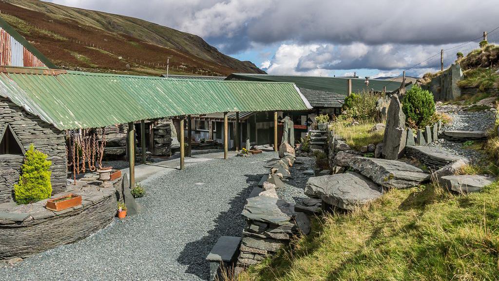 The visitor centre at the slate mine at Honister Pass. It's a small building made of slate, with a sloping corrugated iron roof propped up by some posts. Chains are hanging from the roof.