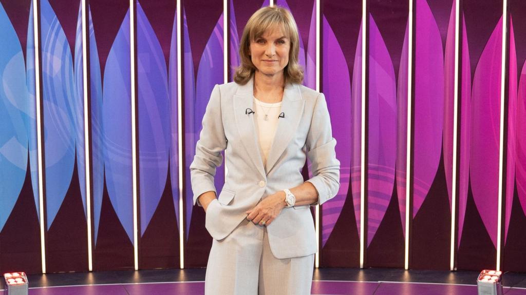 The BBC's Fiona Bruce stands in front of a colourful background, wearing a grey suit (file photo)