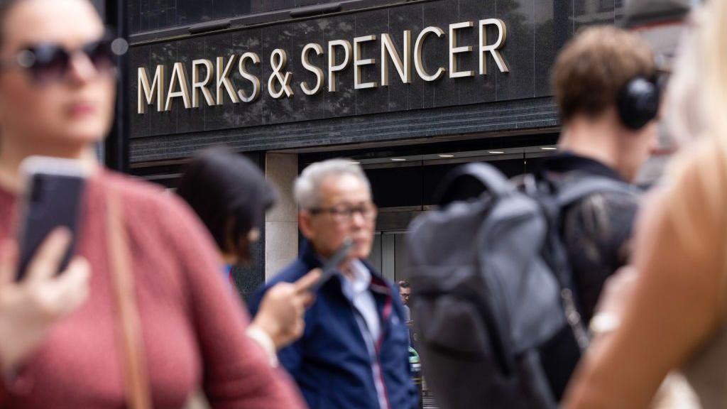 People walking in front of Marks and Spencer store front.