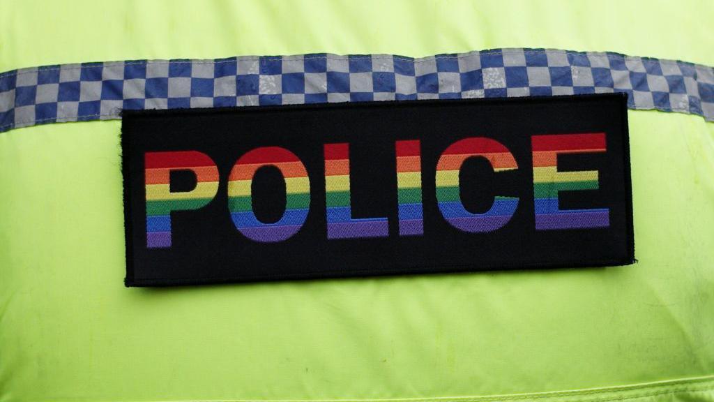 A Northumbria Police officer wearing a Pride badge. The badge is a black rectangle with the word POLICE written in the colours of the rainbow flag.