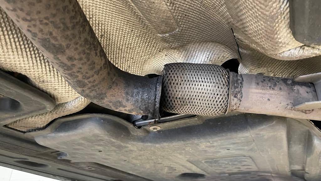 The exhaust pipe of a car with part of the pipe dislodged and showing a gap between the parts underneath the car.