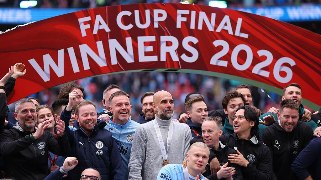 Pep Guardiola stands with the team as they celebrate winning the FA Cup.