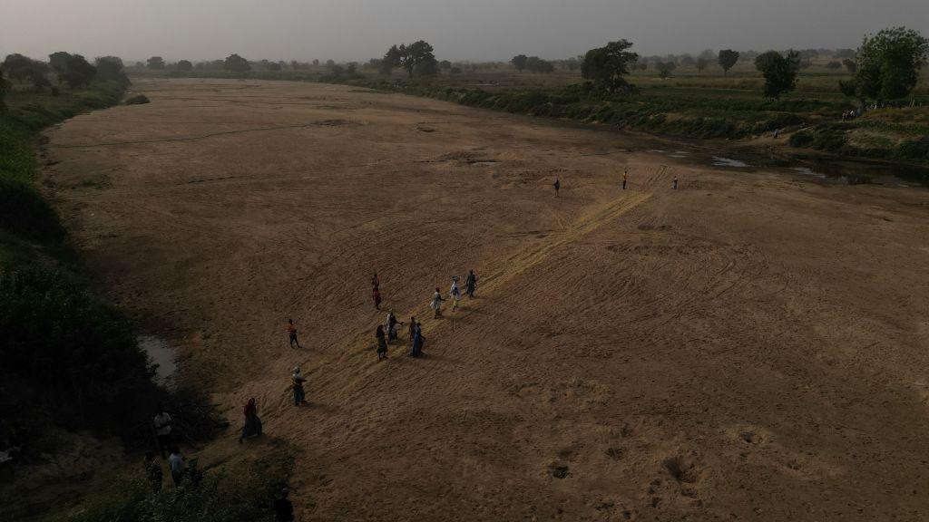 This aerial view shows refugee women crossing the dry beds of the White Volta river to their farms in Burkina Faso from Issakateng-Bausi, in Bawku, northern Ghana, on 7 December 2022