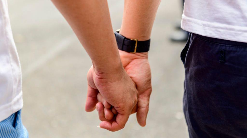 Two people holding hands. One has a watch on his wrist.