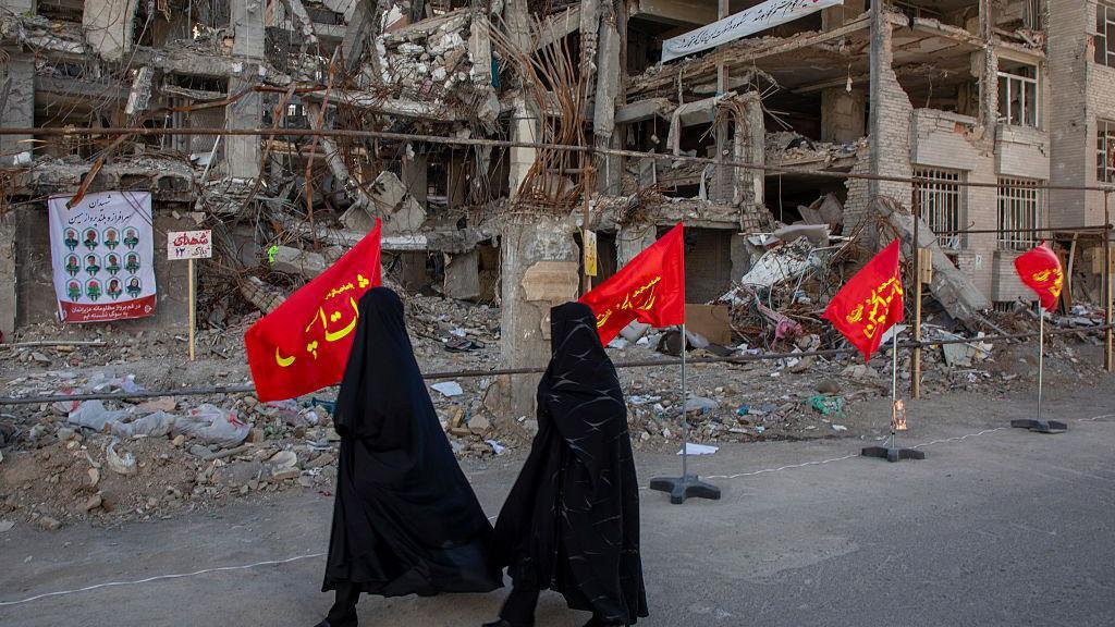 Women walk in front of a damaged building in Tehran
