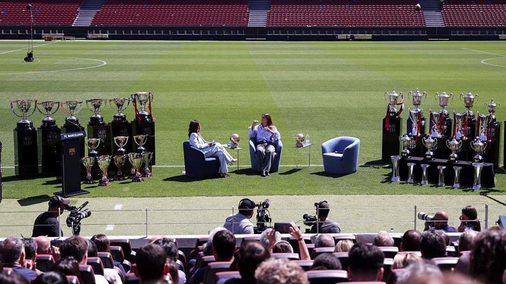 Alexia Putellas sits down with an interviewer at the Camp Nou with 19 trophies on both sides of her