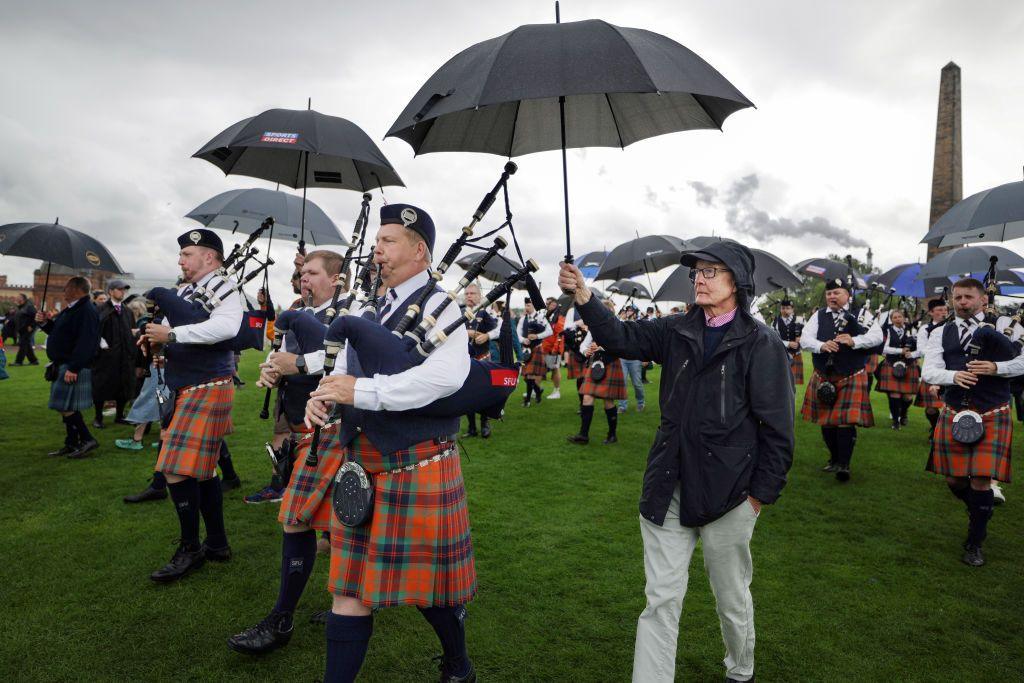 Men playing the bagpipes with umbrellas being held over them. 