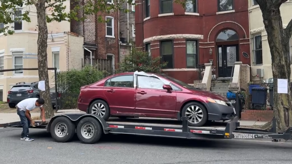A red car with a smashed window is on a trailer