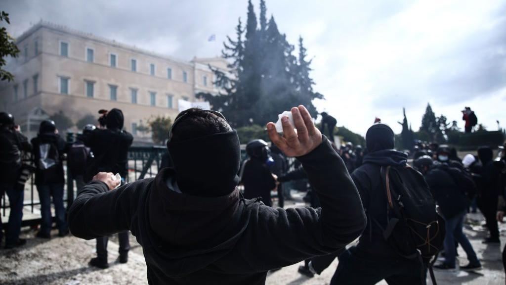 A man holds a stone during clashes in the centre of Athens, his back towards the camera