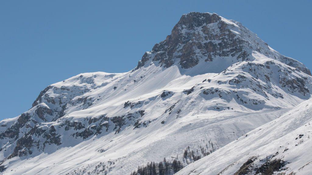 A snow-covered mountain slope with ski tracks leading into a pristine, off-piste area under a clear blue sky.