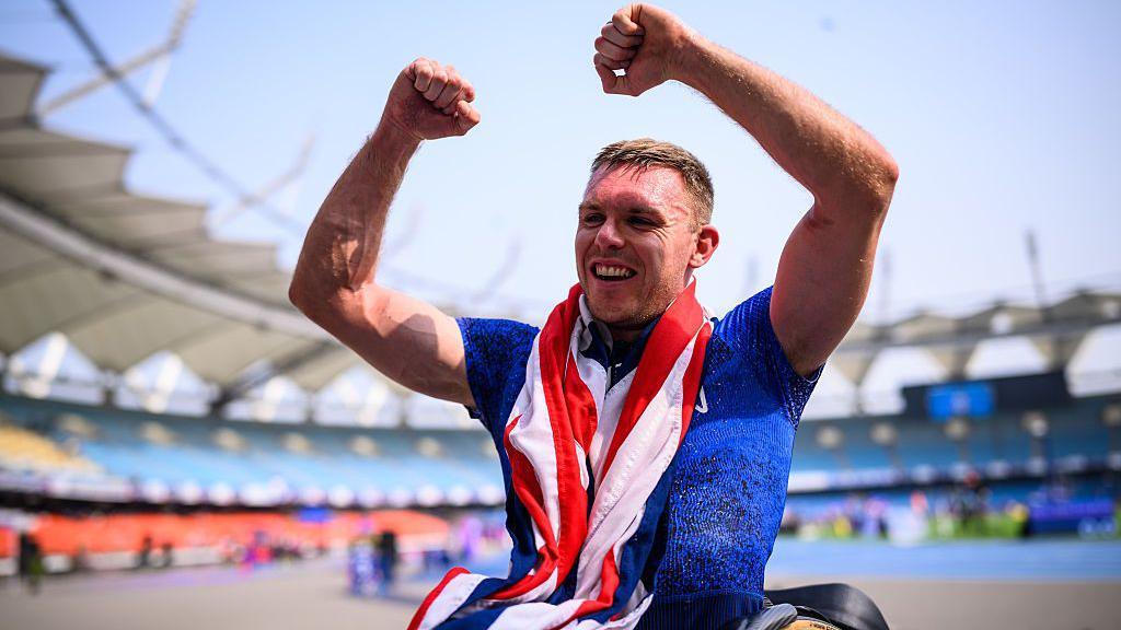 Nathan Maguire has a Union Jack draped around his neck and holds up his arms