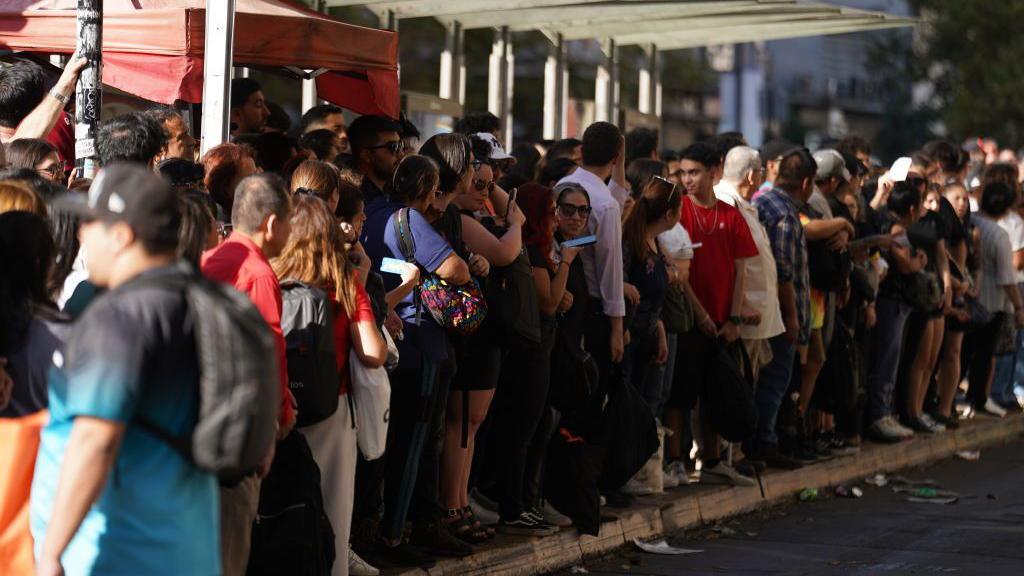 A large group of people can be seen waiting at a bus stop in Santiago, on February 25, 2025. 