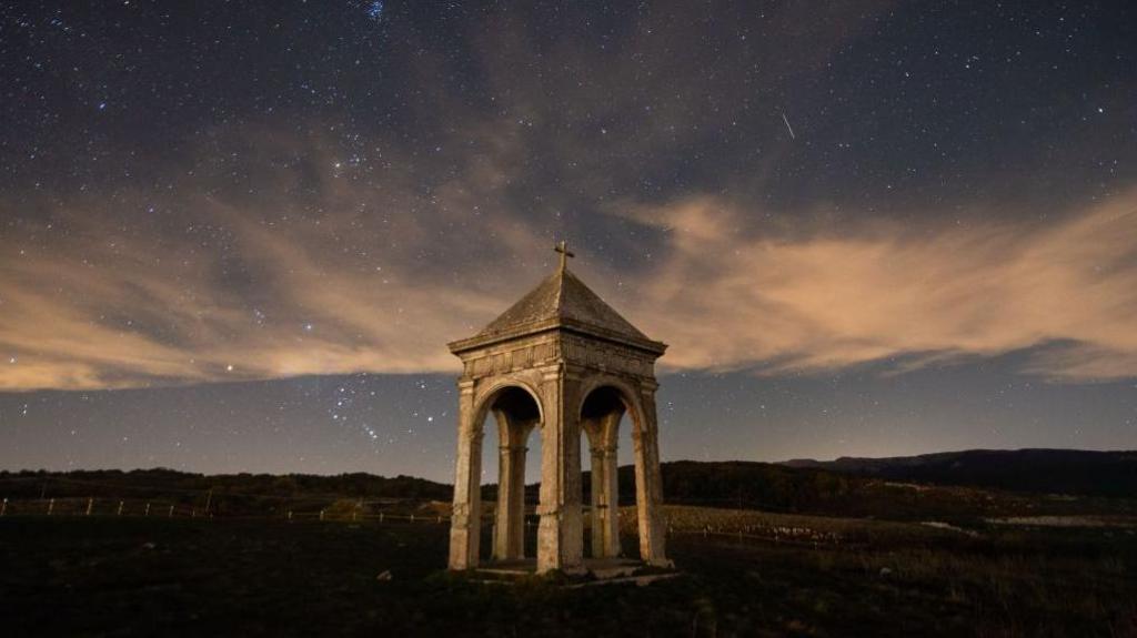 A starry night sky with meteor trails above a stone building in an Italian countryside landscape
