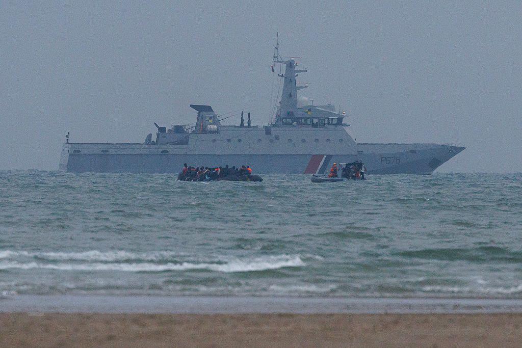 A view of the sea from the beach. A large ship in the distance, with two small dinghies carrying people in the foreground.