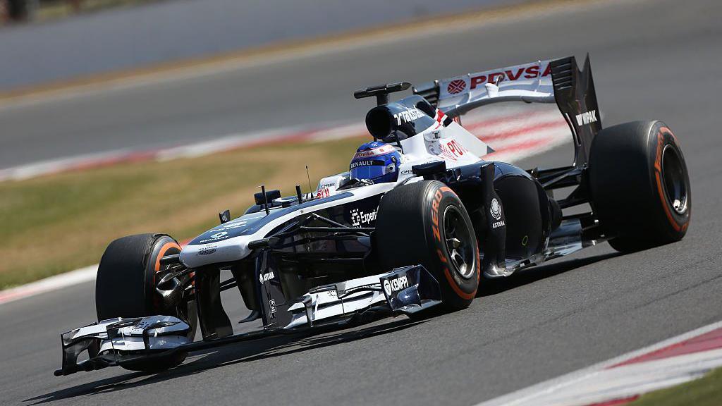 A Williams Formula 1 car, in blue and white livery, speeding around the track at Silverstone. It is moving from right to left in the image.