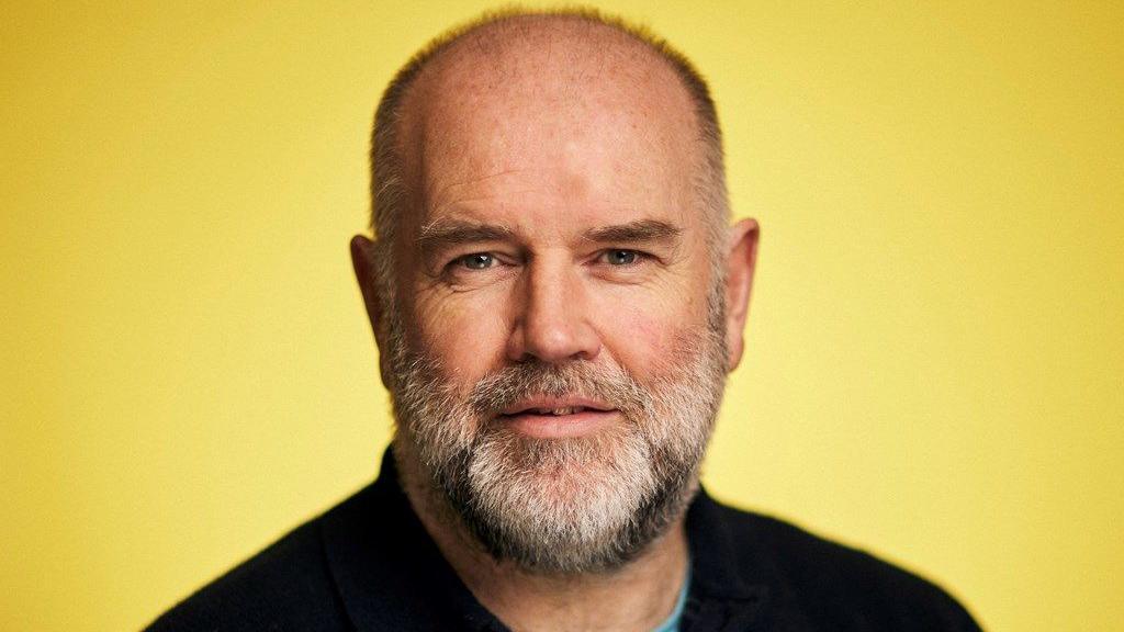 Photographic portrait of Stan Gilmour against a yellow background