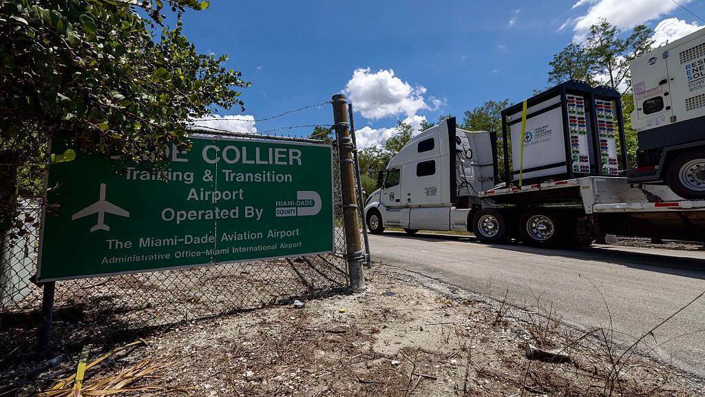 A truck carrying generators drives past a sign saying 'Collier'