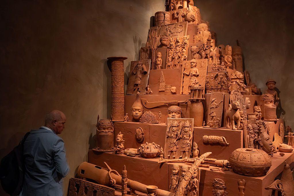Someone looking at Yinka Shonibare's Monument to the Restitution of the Mind and Soul - a pyramid-shaped unit featuring more than 150 clay replicas of the Benin Bronzes.
