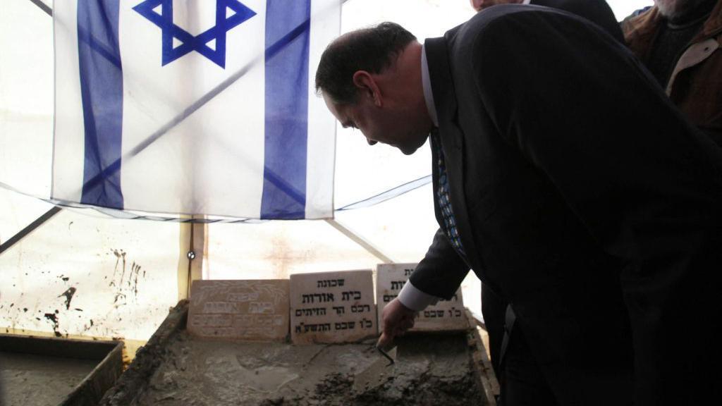 Former Arkansas governor Mike Huckabee adds concrete to a corner stone in front of an Israeli flag during a dedication ceremony for a new Israeli settlement at Beit Orot, in occupied East Jerusalem on 31 January 2011.