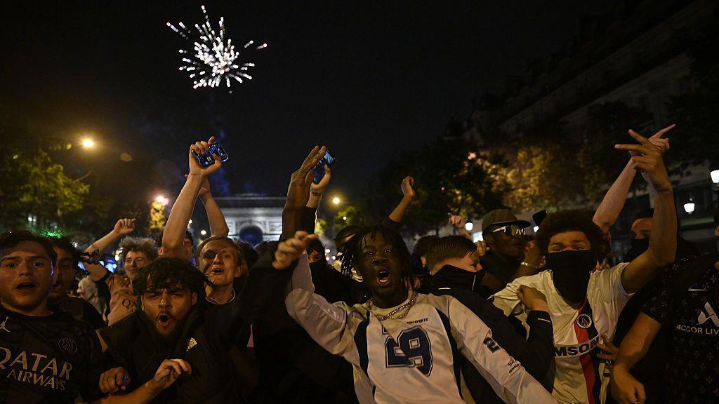 A group of celebrating football fans with the Arc de Triomphe visible in the background