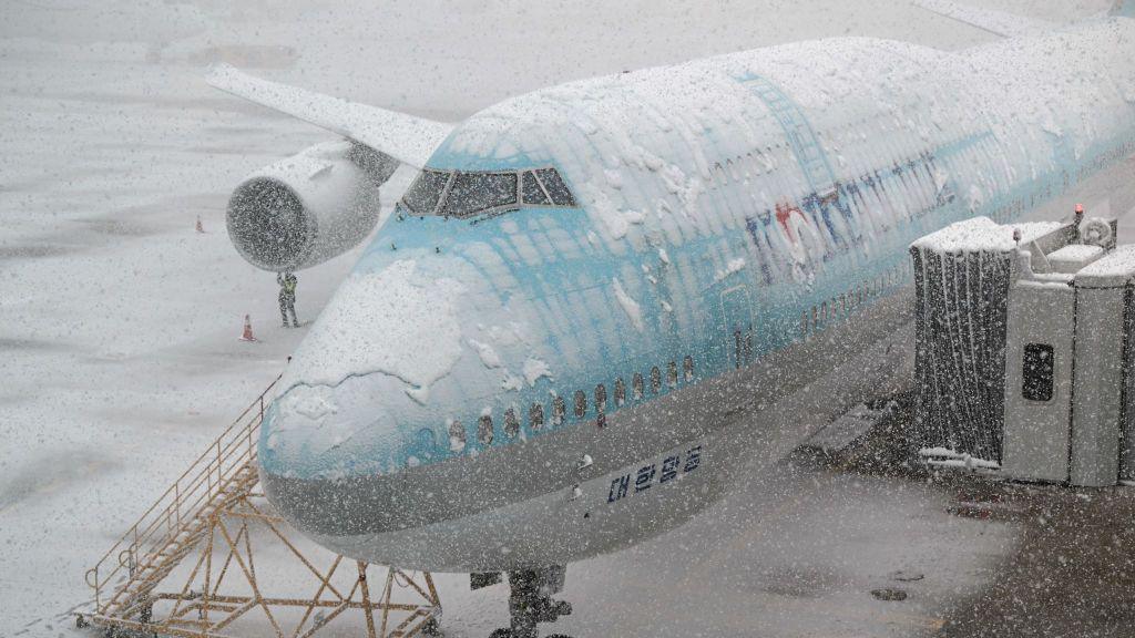 A worker checks a blue snow-covered Korean Air plane parked on the tarmac during snowfall as seen through a window at Incheon international airport, west of Seoul.