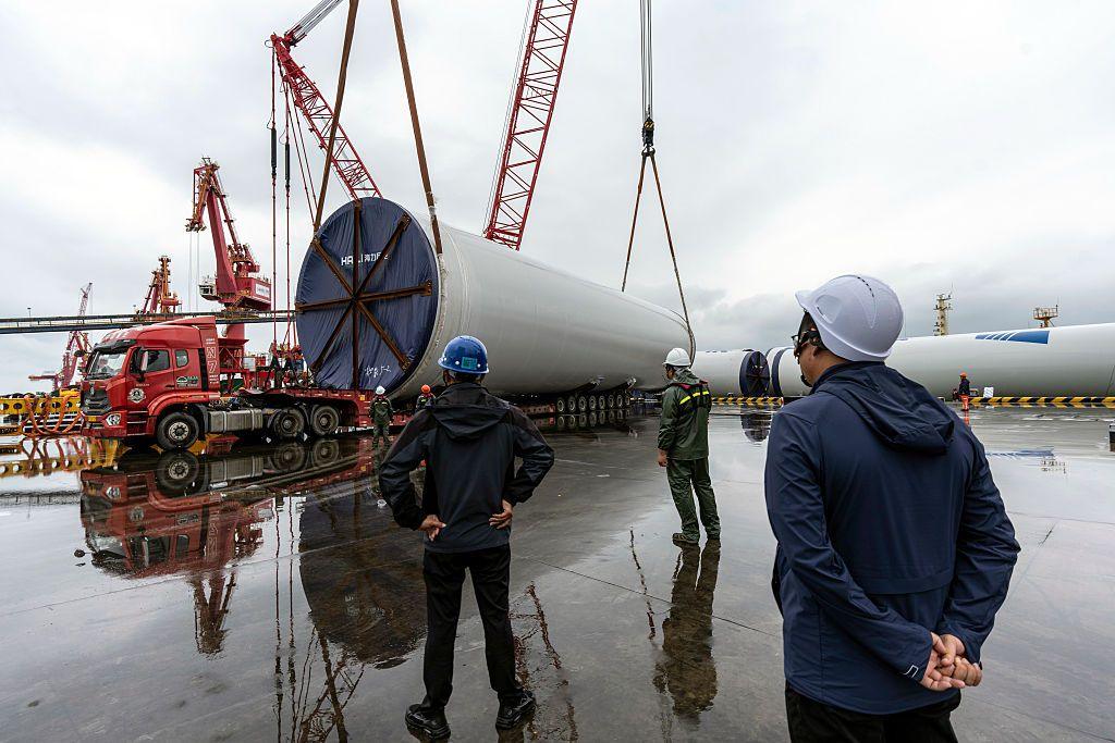 Workers in hard hats watch on as a wind turbine is loaded onto a large lorry
