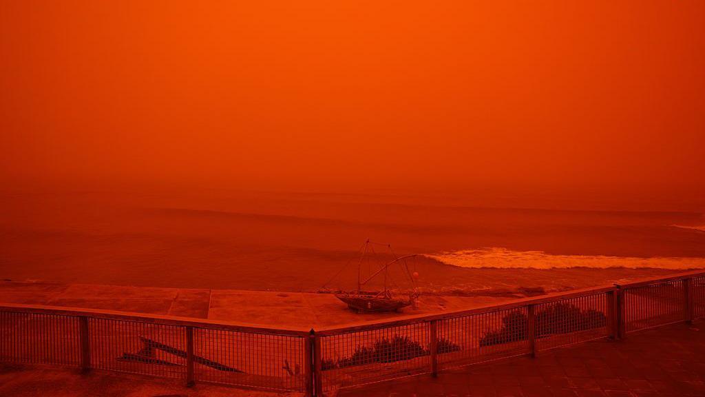 saharan dust storm red sky by sea.