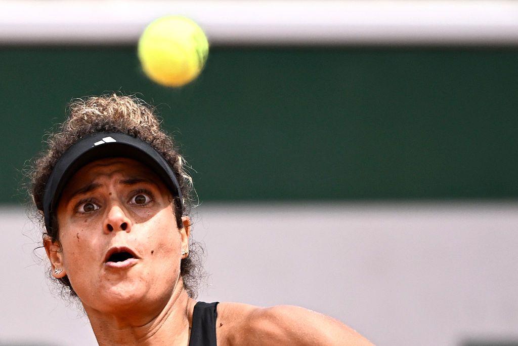 A woman wearing a tennis visor stares intently at the ball as she prepares to strike it with her racket.