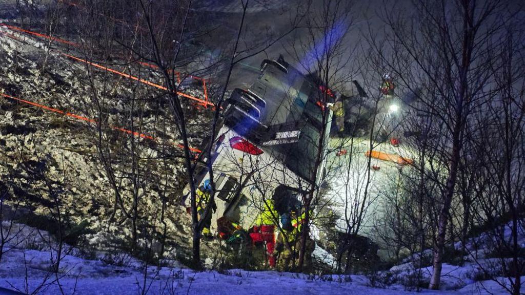 Emergency service staff gathered around an overturned bus in the snow