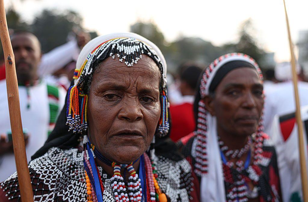 Women and mean wearing beaded jewellery and clothing stand together.
